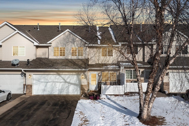 multi unit property featuring aphalt driveway, brick siding, roof with shingles, covered porch, and an attached garage