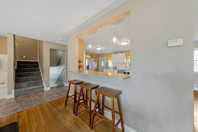 kitchen featuring dark wood finished floors, stainless steel refrigerator with ice dispenser, a breakfast bar area, white cabinetry, and a peninsula