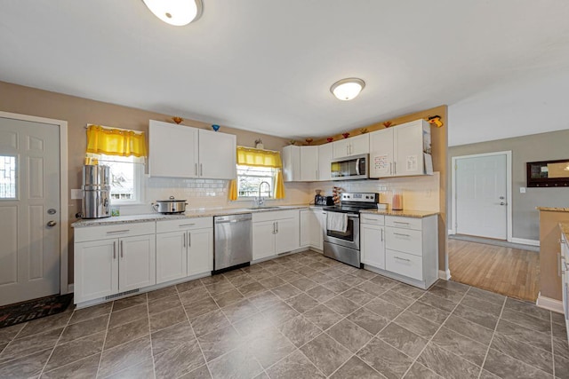 kitchen featuring tasteful backsplash, appliances with stainless steel finishes, white cabinetry, a sink, and baseboards