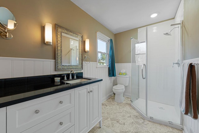 full bathroom featuring a stall shower, wainscoting, vanity, and toilet