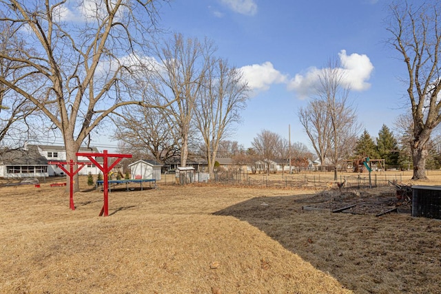 view of yard featuring a trampoline, a playground, and fence