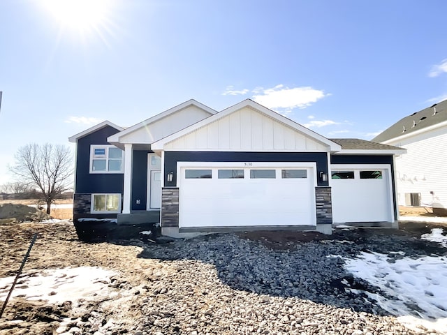 view of front of house featuring board and batten siding, gravel driveway, central AC unit, a garage, and stone siding