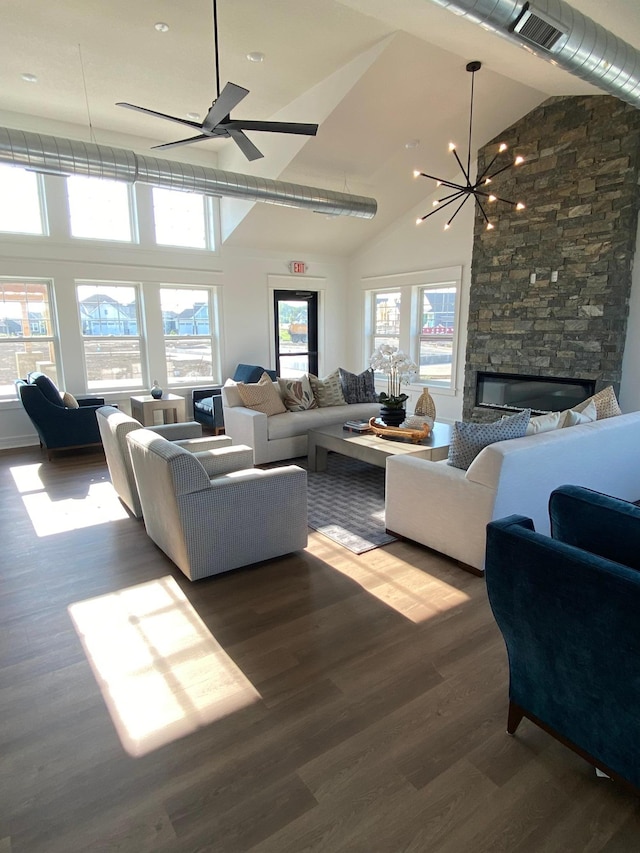 living area with wood finished floors, visible vents, high vaulted ceiling, a stone fireplace, and ceiling fan with notable chandelier