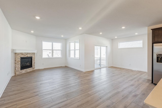 unfurnished living room featuring recessed lighting, light wood-style flooring, baseboards, and a glass covered fireplace