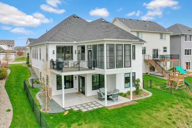 rear view of house with a patio area, a lawn, a playground, and roof with shingles