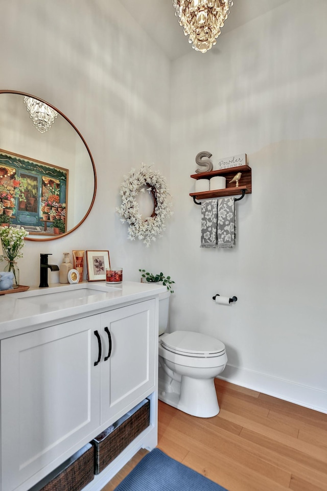 half bathroom with baseboards, toilet, wood finished floors, an inviting chandelier, and vanity