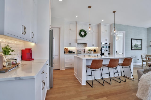 kitchen featuring double oven, light wood-style flooring, white cabinets, and a kitchen breakfast bar