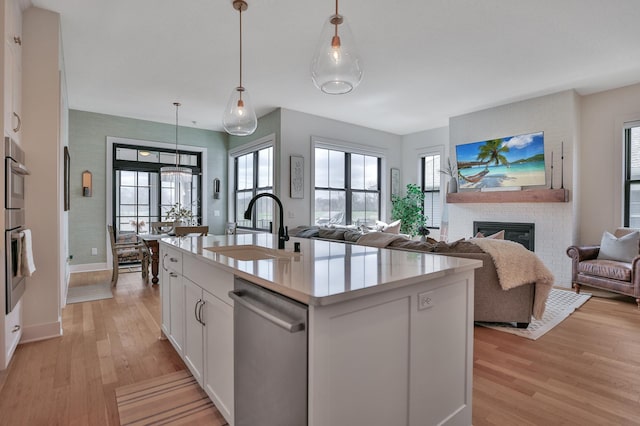 kitchen featuring light wood-style flooring, light countertops, stainless steel dishwasher, a fireplace, and a sink