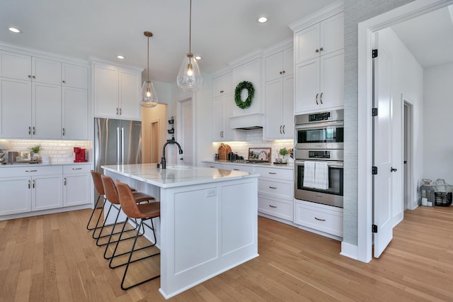 kitchen featuring a sink, white cabinets, a kitchen breakfast bar, light countertops, and appliances with stainless steel finishes