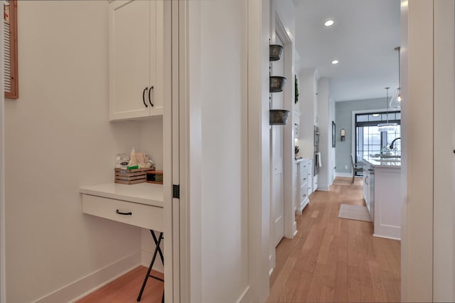 corridor with recessed lighting, light wood-type flooring, a sink, and baseboards