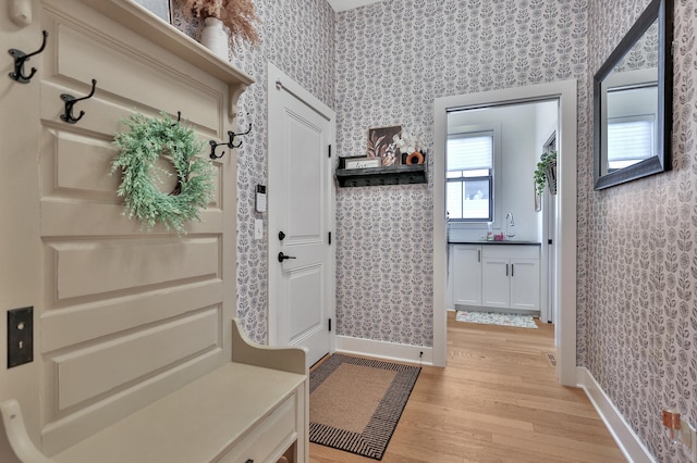 mudroom featuring light wood-type flooring, wallpapered walls, baseboards, and a sink