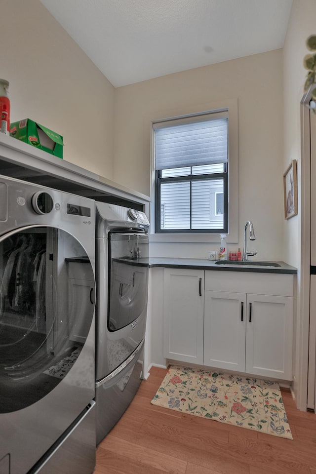 laundry area featuring cabinet space, a sink, washer and clothes dryer, and light wood finished floors