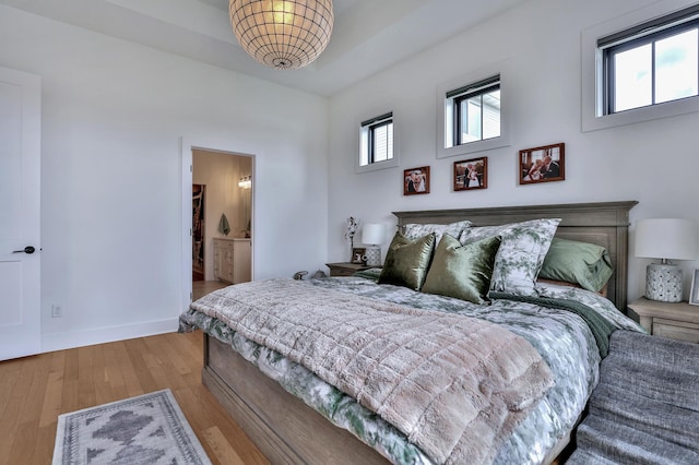 bedroom with ensuite bath, wood finished floors, and baseboards