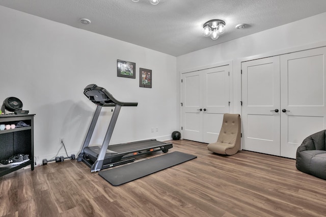 workout room featuring a textured ceiling, baseboards, and wood finished floors