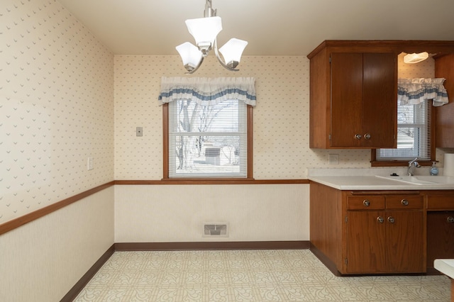 kitchen with light floors, light countertops, wainscoting, a sink, and wallpapered walls