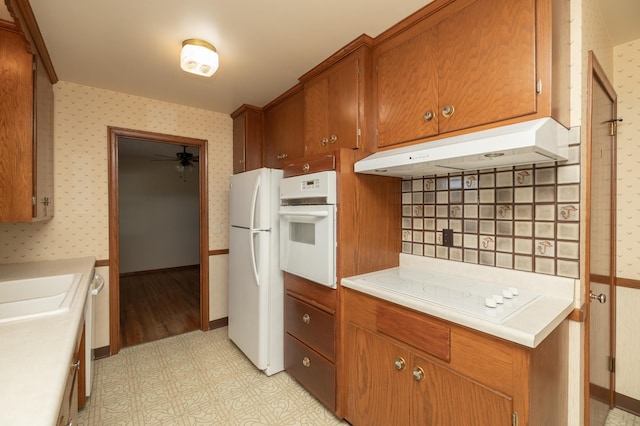 kitchen featuring white appliances, wallpapered walls, light floors, light countertops, and under cabinet range hood