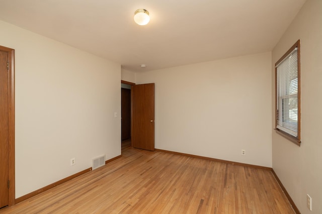 empty room with baseboards, visible vents, and light wood finished floors