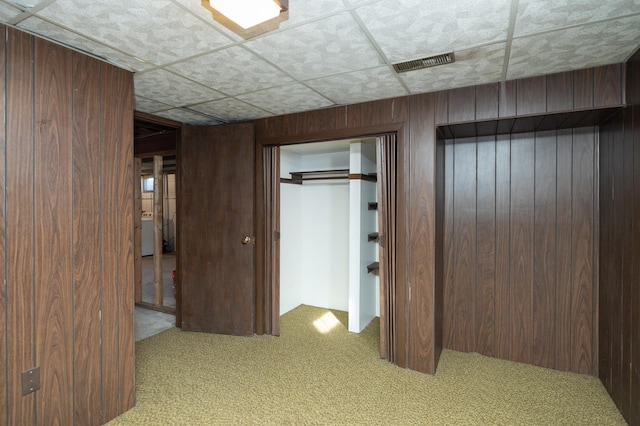 interior space featuring carpet flooring, visible vents, wood walls, and a drop ceiling