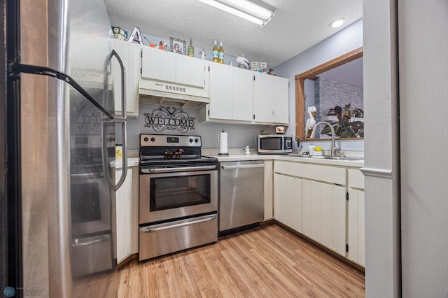 kitchen featuring light wood-style flooring, stainless steel appliances, light countertops, under cabinet range hood, and a sink