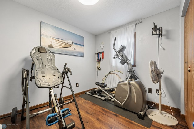 exercise area with a textured ceiling, baseboards, and wood finished floors