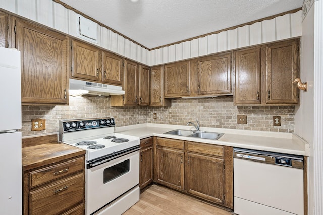 kitchen with decorative backsplash, a sink, a textured ceiling, white appliances, and under cabinet range hood