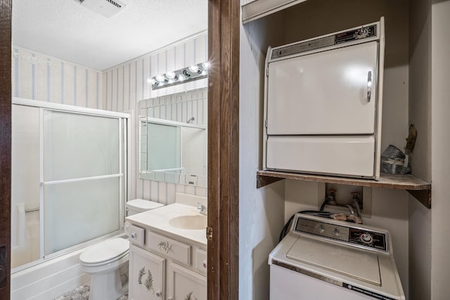 bathroom featuring enclosed tub / shower combo, toilet, visible vents, vanity, and stacked washing maching and dryer