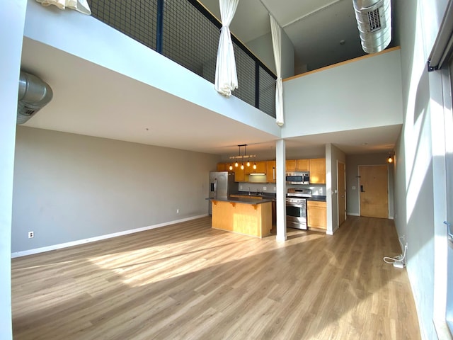 kitchen featuring baseboards, dark countertops, light wood-style flooring, appliances with stainless steel finishes, and open floor plan