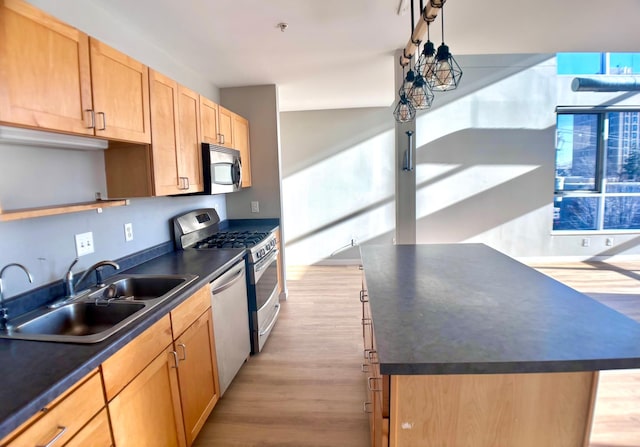 kitchen with dark countertops, light wood-style flooring, stainless steel appliances, and a sink