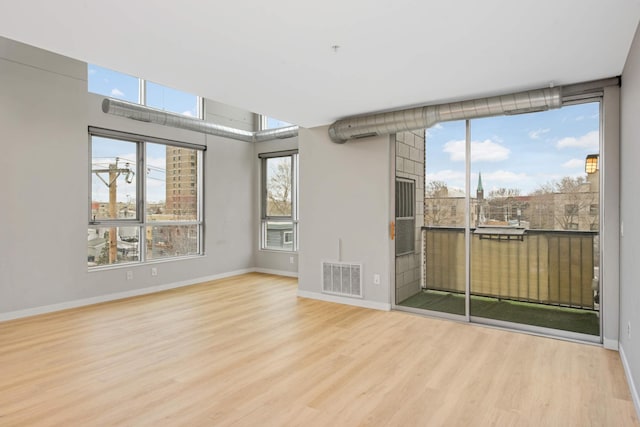 empty room with wood finished floors, visible vents, and a healthy amount of sunlight