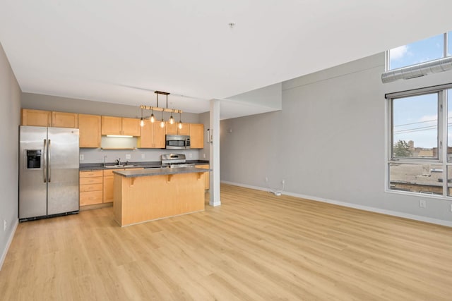 kitchen with light brown cabinetry, dark countertops, baseboards, appliances with stainless steel finishes, and a breakfast bar area