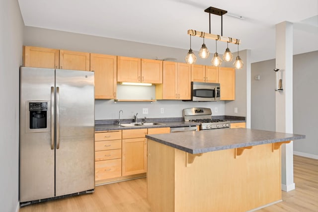 kitchen featuring light brown cabinetry, stainless steel appliances, dark countertops, a sink, and light wood-style flooring