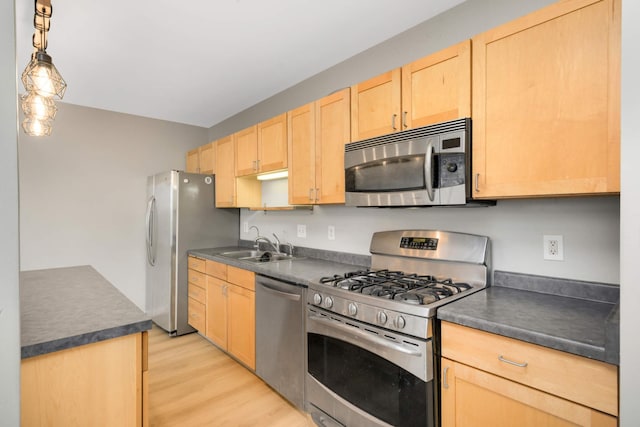 kitchen featuring light brown cabinets, dark countertops, a sink, light wood-style floors, and stainless steel appliances