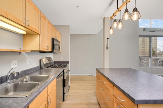 kitchen featuring light wood finished floors, a sink, dark countertops, baseboards, and appliances with stainless steel finishes