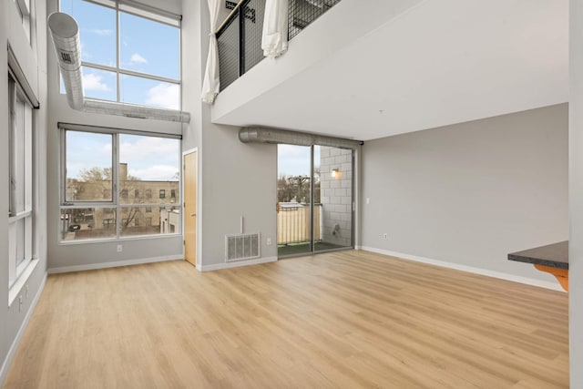 unfurnished living room with baseboards, wood finished floors, visible vents, and a healthy amount of sunlight