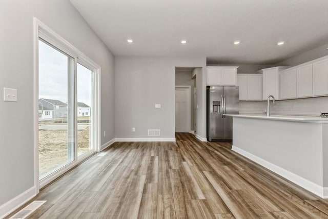 kitchen with light wood finished floors, baseboards, stainless steel fridge with ice dispenser, light countertops, and white cabinetry