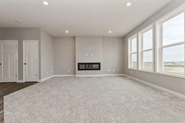 unfurnished living room featuring carpet, recessed lighting, baseboards, and a glass covered fireplace