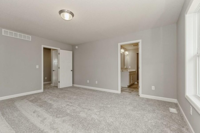 unfurnished bedroom with light carpet, ensuite bath, baseboards, and visible vents