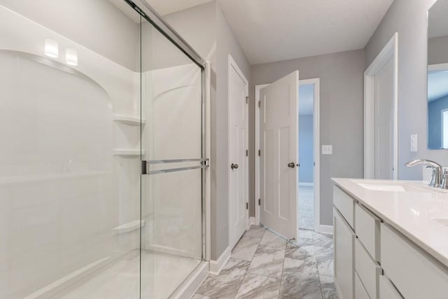 full bathroom with marble finish floor, double vanity, a sink, a shower stall, and baseboards