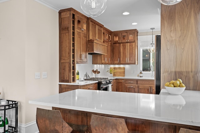 kitchen featuring glass insert cabinets, stainless steel appliances, brown cabinetry, decorative light fixtures, and crown molding