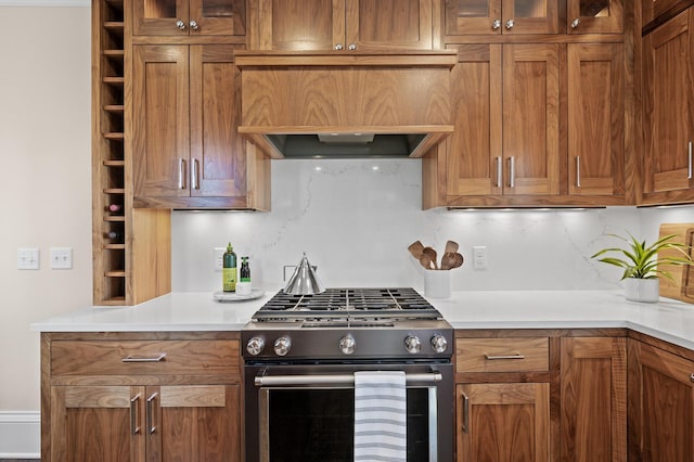 kitchen featuring glass insert cabinets, brown cabinets, light countertops, premium range hood, and stainless steel range with gas stovetop