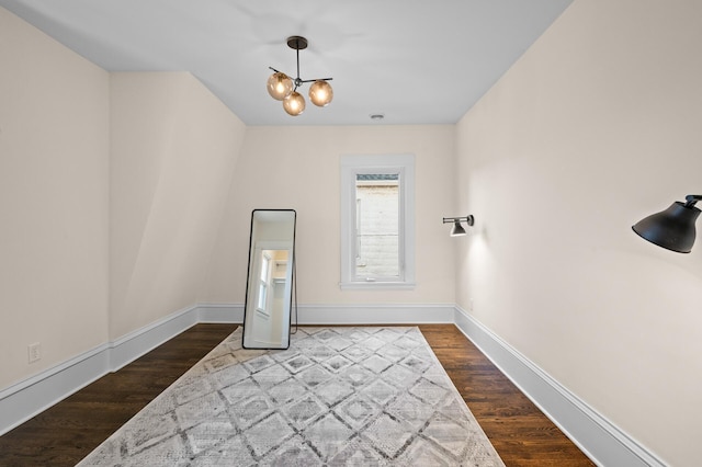 spare room with a chandelier, wood finished floors, and baseboards