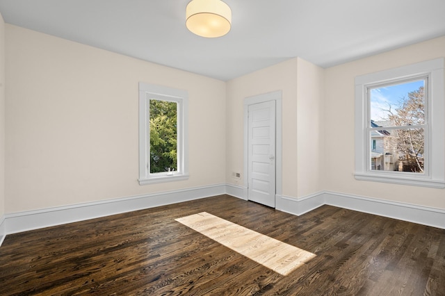 unfurnished bedroom with multiple windows, dark wood finished floors, and baseboards