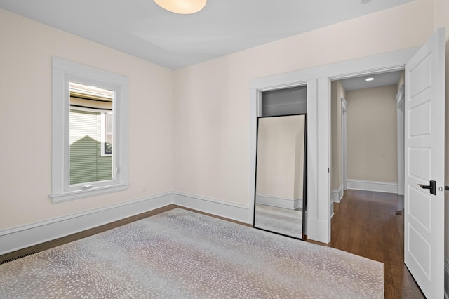 unfurnished bedroom featuring dark wood-style floors, baseboards, and a closet