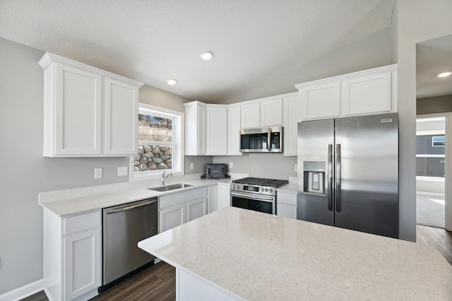 kitchen with lofted ceiling, a sink, white cabinets, appliances with stainless steel finishes, and dark wood finished floors