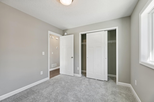 unfurnished bedroom with baseboards, visible vents, a textured ceiling, carpet floors, and a closet