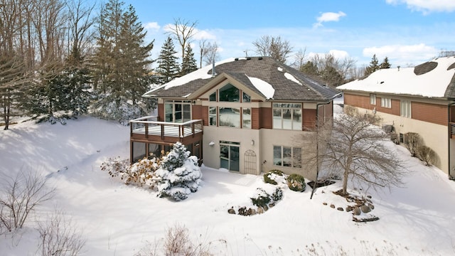 snow covered rear of property with a balcony and stucco siding