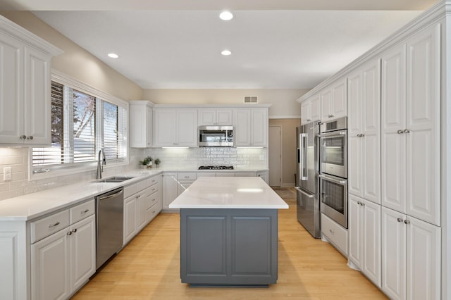 kitchen with appliances with stainless steel finishes, a sink, white cabinets, and a center island