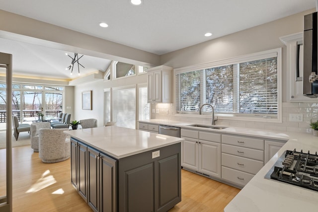 kitchen with decorative backsplash, appliances with stainless steel finishes, white cabinets, a sink, and light wood-type flooring