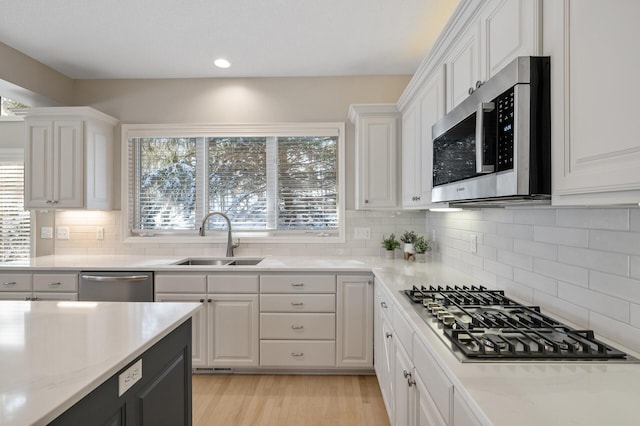 kitchen with light wood-style flooring, a sink, stainless steel appliances, white cabinetry, and backsplash