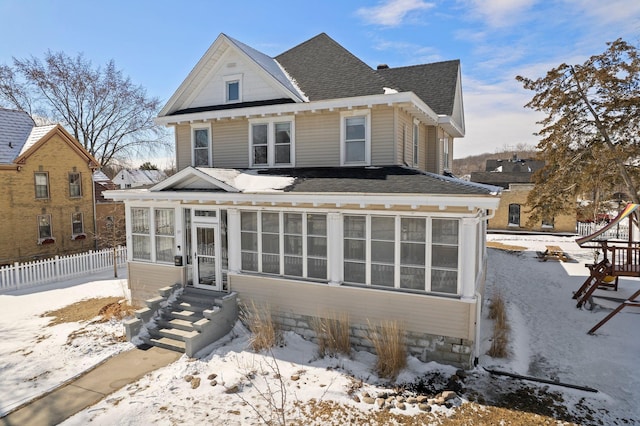 view of front facade with a sunroom, roof with shingles, and fence